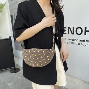 Brown suede crescent bag with gold studs and grommets worn by a model in a street setting
