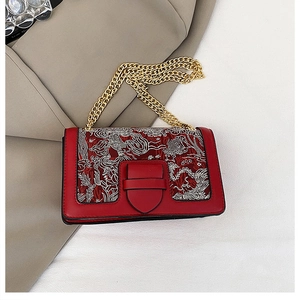 Detail of red leather shoulder bag featuring intricate phoenix embroidery and gold chain