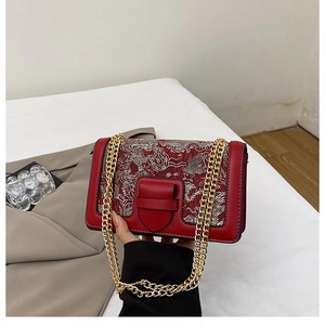 Detail of red crossbody bag with white cloud embroidery and heart-shaped buckle