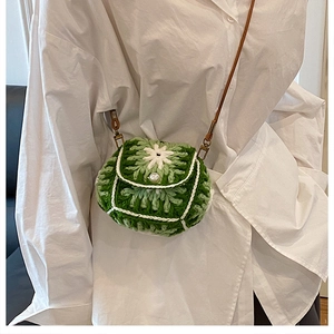 Detail of green knitted crossbody bag with white flower pattern and pearl button closure