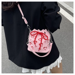 Detail of pink corduroy bucket bag with red heart embroidery and chain strap on model
