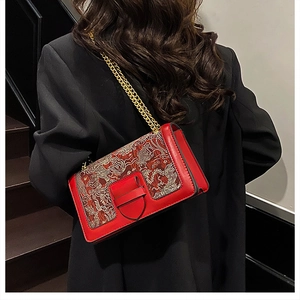 Detail of red leather shoulder bag with vintage embroidery and golden chain strap