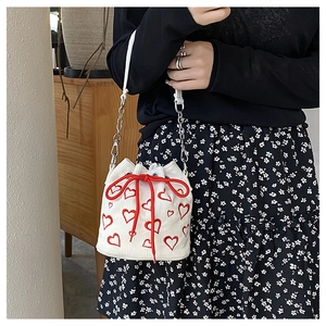 Model showing white corduroy bucket bag with red heart embroidery and chain strap