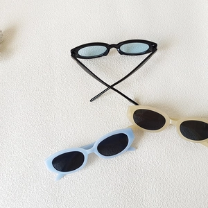 Lunettes de soleil vintage enfant en noir, bleu et crème sur fond texturé blanc