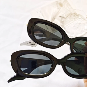Lunettes de soleil rétro à monture ovale noire et verres foncés sur tissu blanc