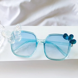 Détail de lunettes de soleil carrées enfant avec verres dégradés bleus et décor papillon