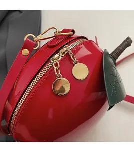 Detailed close-up of glossy red apple crossbody bag with gold dual zippers and green leaf