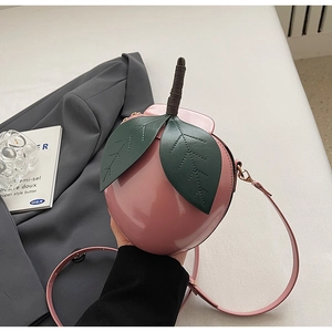 Close-up of pink peach-shaped shoulder bag with green leaf detail and woven strap