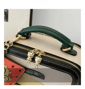 Close-up of golden bear zipper pulls and dark green handle on a retro contrast crossbody bag