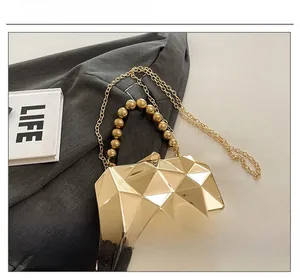 Detail of golden geometric evening bag with metallic bead handle and fine chain strap