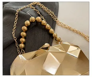 Detail of a geometric golden evening bag with beaded handle and fine chain strap