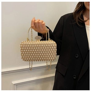 Detail of white pearls and golden handle on evening bag held by a model in a black suit