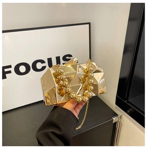 Detailed close-up of golden metallic geometric clutch with ball handle and chain strap