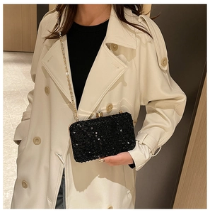 Detail of elegant black sequin evening bag with gold chain strap on a beige trench coat