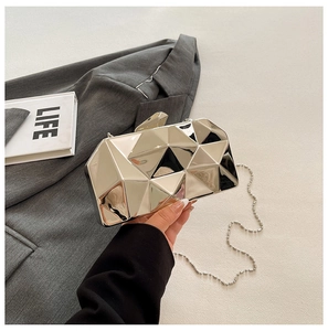 Macro detail of silver geometric evening bag with mirror-finish facets and chain strap
