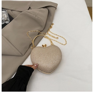Macro view of glittering heart-shaped gold evening bag with metal ring handle and chain