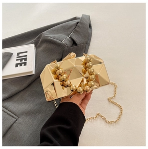 Macro detail of golden geometric evening bag with bead handle and metallic chain strap