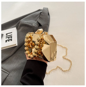 Close-up of golden geometric hard shell clutch bag with beaded handle and chain strap