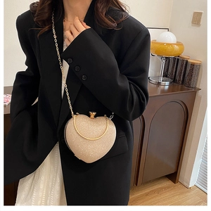 Champagne glitter heart-shaped evening bag with gold chain strap held by a model