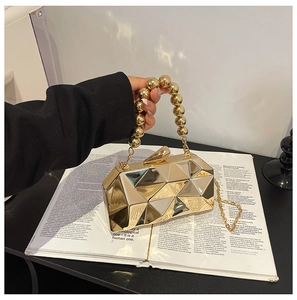 Detail of gold geometric metal clutch bag with beaded handle and chain strap on magazine