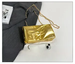 Detail of gold metallic textured crossbody bag with chain next to smartphone for size comparison