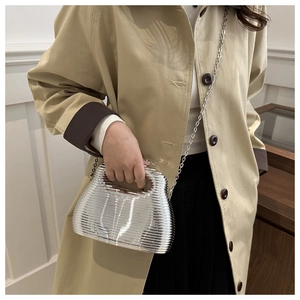 Detail of silver wavy acrylic evening bag with chain strap held by a model in a trench coat