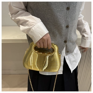 Detail of gold wavy evening bag with top handle and metallic chain strap on model