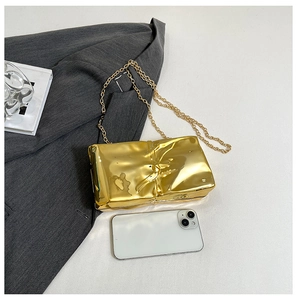 Detail of gold liquid metal textured crossbody bag with fine chain on grey suit
