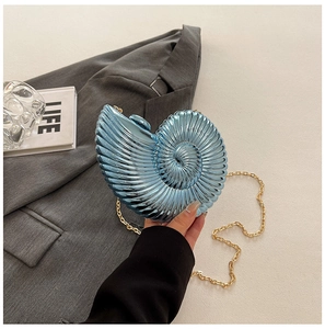 Detail of blue nautilus-shaped shell clutch bag with gold chain strap held by model