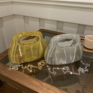 Golden and silver acrylic wave clutch bags with metal chain on a coffee table