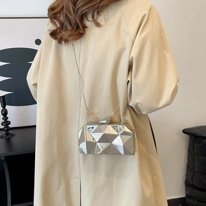 Silver geometric hard shell evening clutch with metal chain shown on a beige trench coat