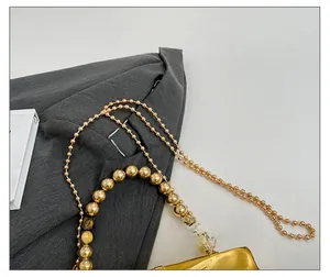 Dettaglio borsa in acrilico specchiato oro con grande manico di perle e tracolla a catena