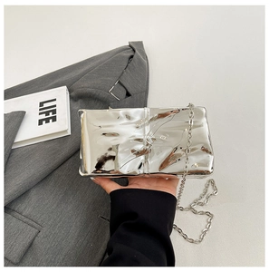 Dettaglio della borsa clutch a specchio argento con pieghe irregolari e catena sottile