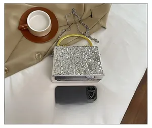 Macro view of silver acrylic box clutch with lava texture and smartphone for scale