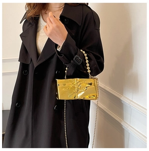 Dettaglio della borsa in acrilico oro metallizzato con manico di perle su modella in nero