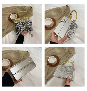 Macro detail of silver acrylic evening box bag with golden dragon handles and mirror texture