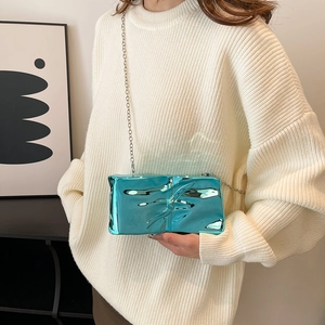 Modern teal metallic acrylic clutch bag with chain strap worn by model in casual style