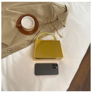 Flat lay of a gold mirror-finish acrylic box clutch with round handle and chain strap