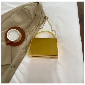 Top view of a gold mirror-finish acrylic box bag with metal handle and chain on a white fabric
