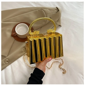 Detail of gold acrylic clutch with vertical stripes and ornate dragon-shaped handles