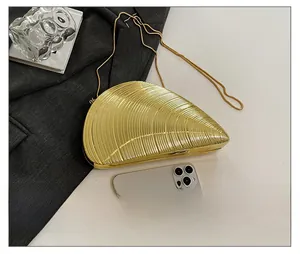 Detail showing the golden conch clutch bag size compared to a smartphone with chain strap