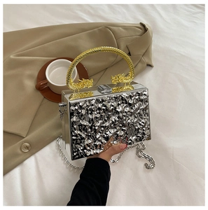 Detail of silver wavy acrylic clutch featuring gold dragon-head handles and metal chain