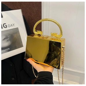 Detail of gold box clutch featuring dragon relief handle and metallic chain strap