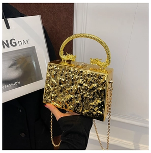 Detail of gold acrylic box clutch featuring dual dragon handles and wavy mirror texture