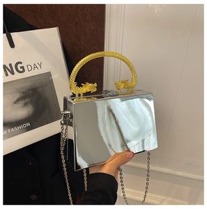 Detail of silver mirror box bag featuring golden dragon handles and metallic chain strap