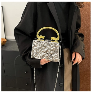 Detail of silver metallic evening clutch with golden dragon handle and chain strap