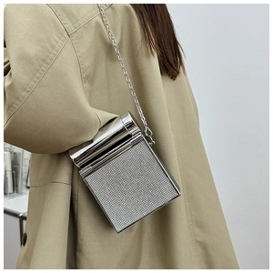 Close-up of a silver rhinestone mini box bag with metal chain on a khaki trench coat