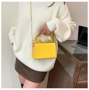 Detail of yellow acrylic evening bag featuring a gold dragon head handle and chain strap