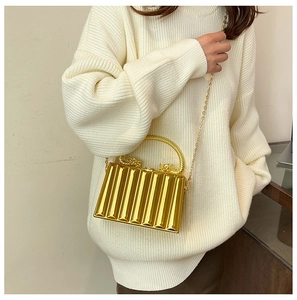 Detail of gold evening box bag with dragon clasp and striped mirror finish on model