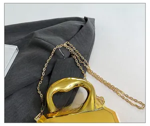 Detail view of golden acrylic geometric clutch with thin metal chain strap and mirror finish